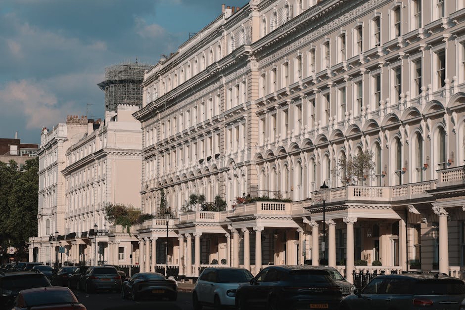 An exterior view of a row of white Victorian-style terraced houses on Ladbroke Grove, featuring ornate cornices, bay windows, and balconies with stone balustrades. Parked cars line the pavement in fro